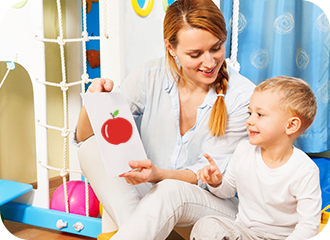 A female teacher is showing an apple image to a kid